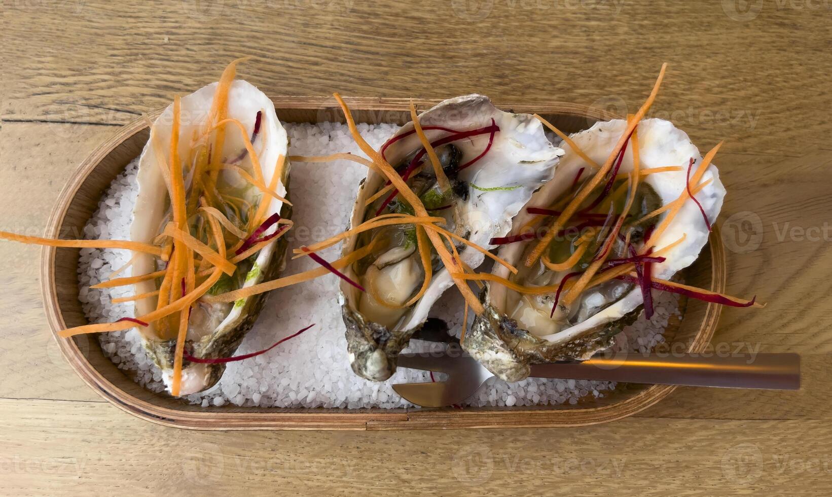 three oysters on a wooden tray with a knife and fork photo