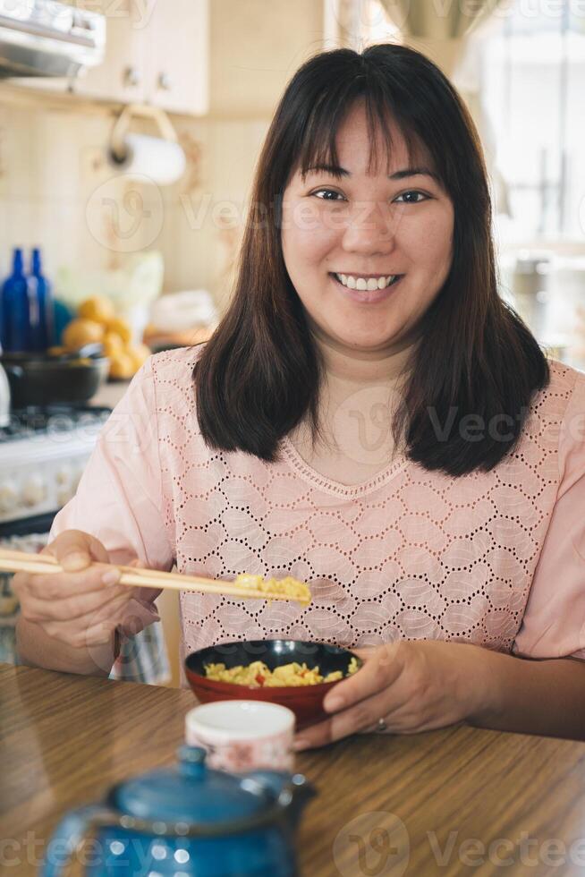 Asian woman eating rice with chopsticks looks and smiles at camera. photo