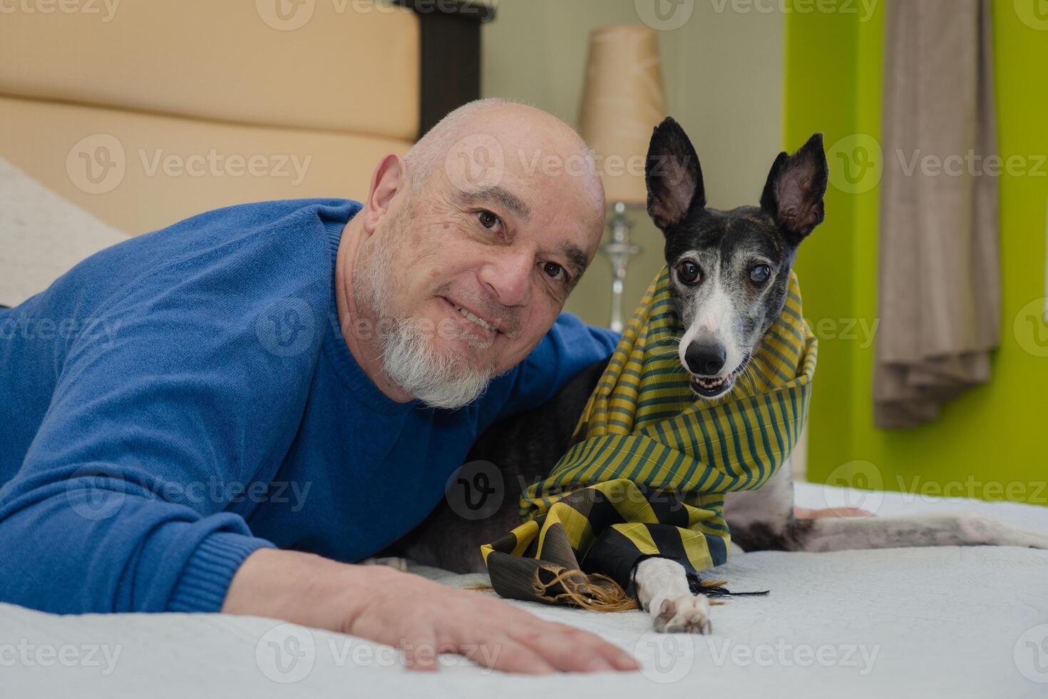 un maduro hombre y su galgo actitud juntos en el cama para el cámara. foto