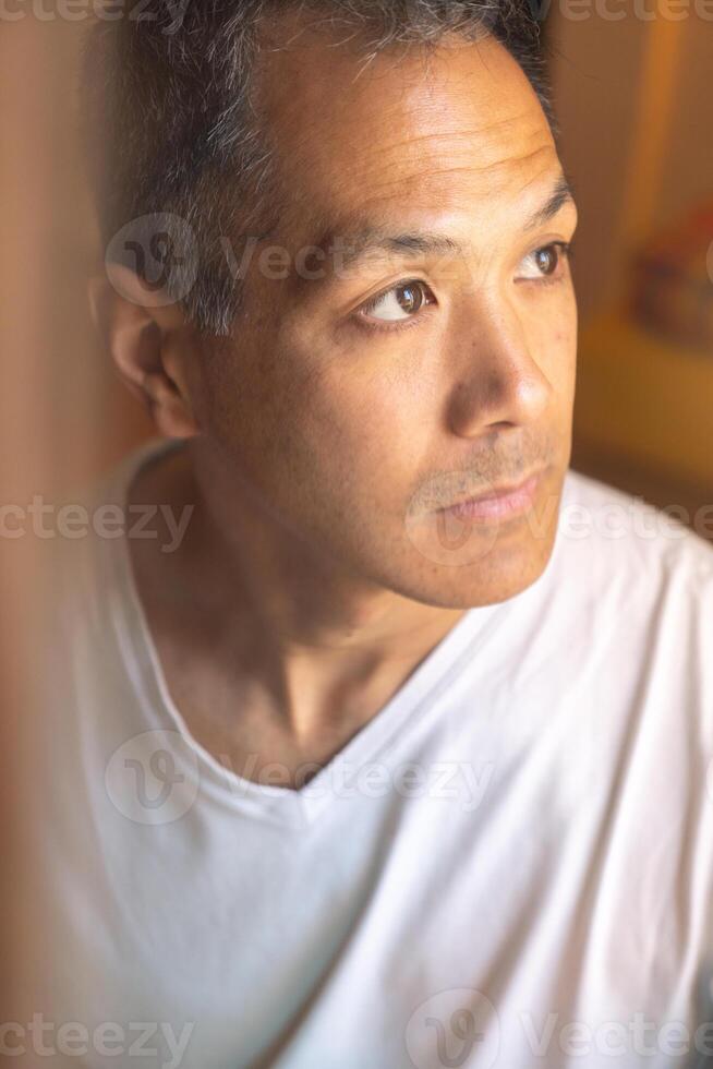 vertical retrato de joven japonés hombre mirando fuera de un ventana con un pensativo expresión. foto