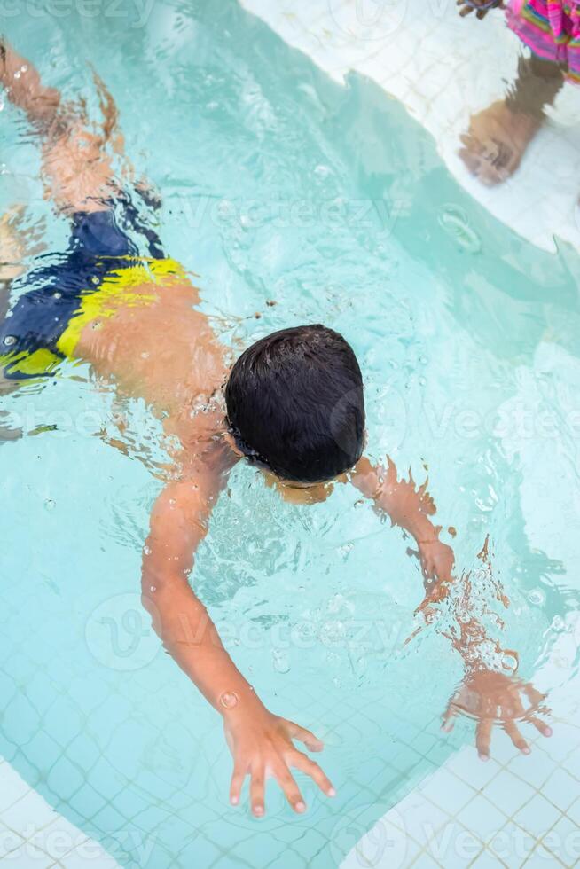 contento indio chico nadando en un piscina, niño vistiendo nadando disfraz a lo largo con aire tubo durante caliente verano vacaciones, niños chico en grande nadando piscina. foto