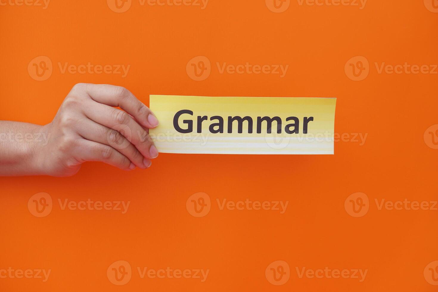 Close up hand holds paper card with text Grammar. Orange background. Concept, education, learning, studying language. Education. Reading and memorizing strategy of learning process. Grammar lesson. photo