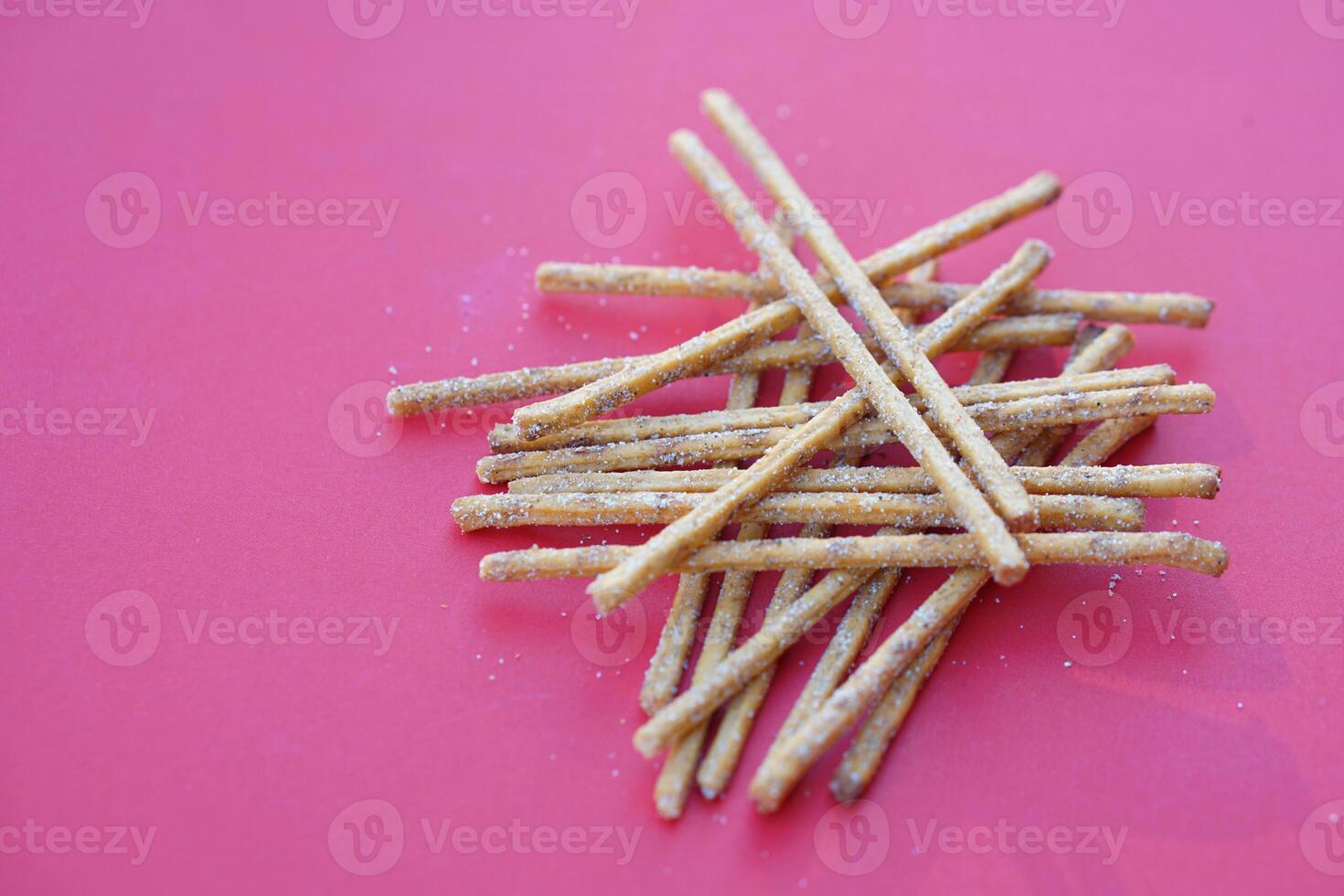 Crunchy salty and spicy flavored pretzel sticks, breadsticks, snacks on red background. Concept, junk food, appetizer. photo