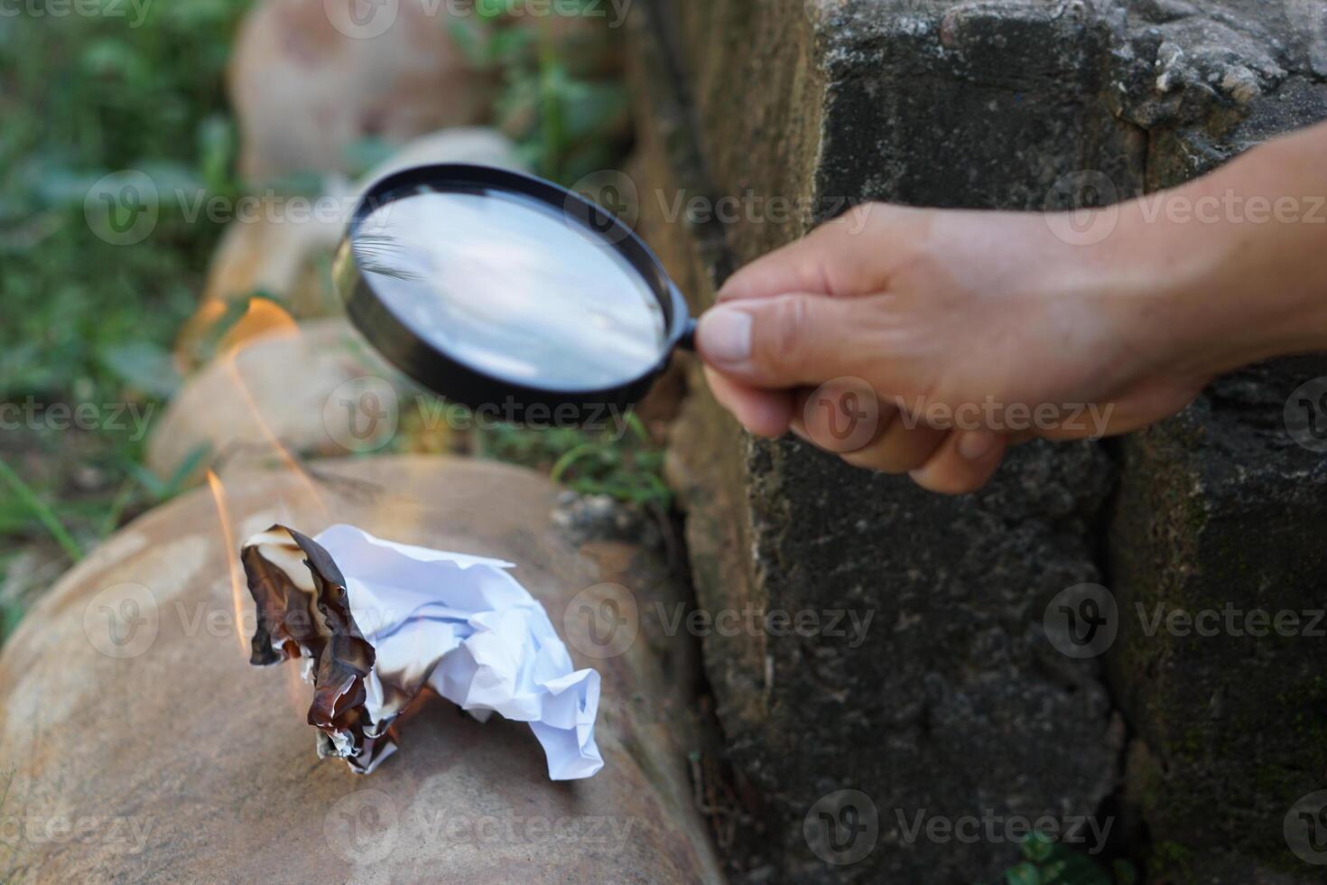 Close up hand hold magnifying glass to make fire for burning paper. Concept, Science experiment about convex lens, hold magnifying glass between the sun and tinder. Handy survival skills. photo