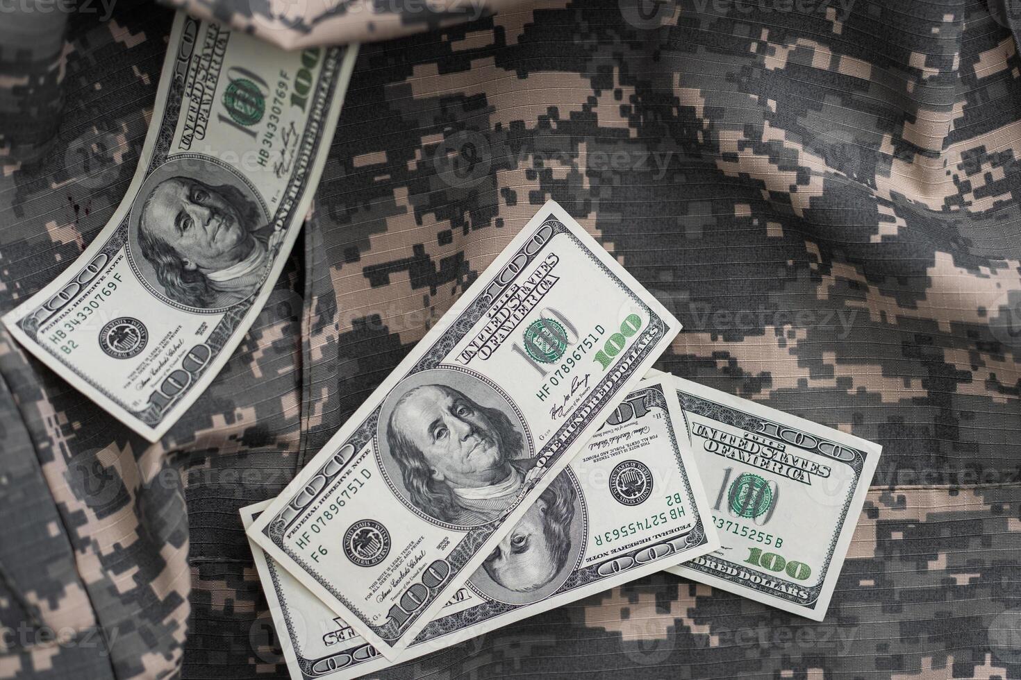 US dollar bills on fabric with texture of Ukrainian military pixeled camouflage. Cloth with camo pattern in grey, brown and green pixel shapes. Official uniform of Ukrainian soldiers close up. photo