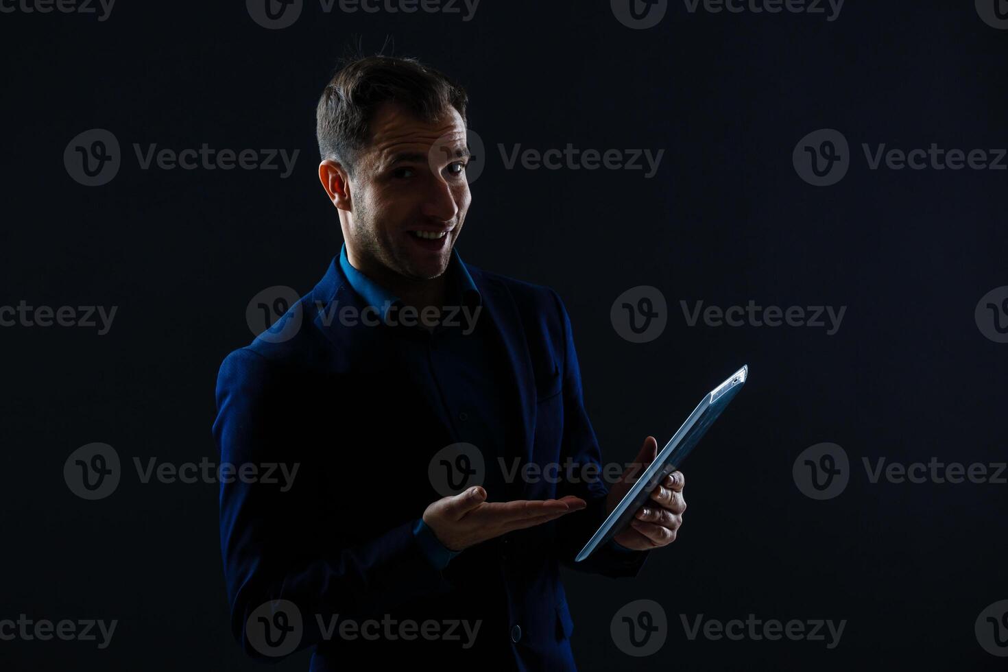 A serious handsome young businessman in a suit using a tablet in front of a dark grey background in a studio. photo