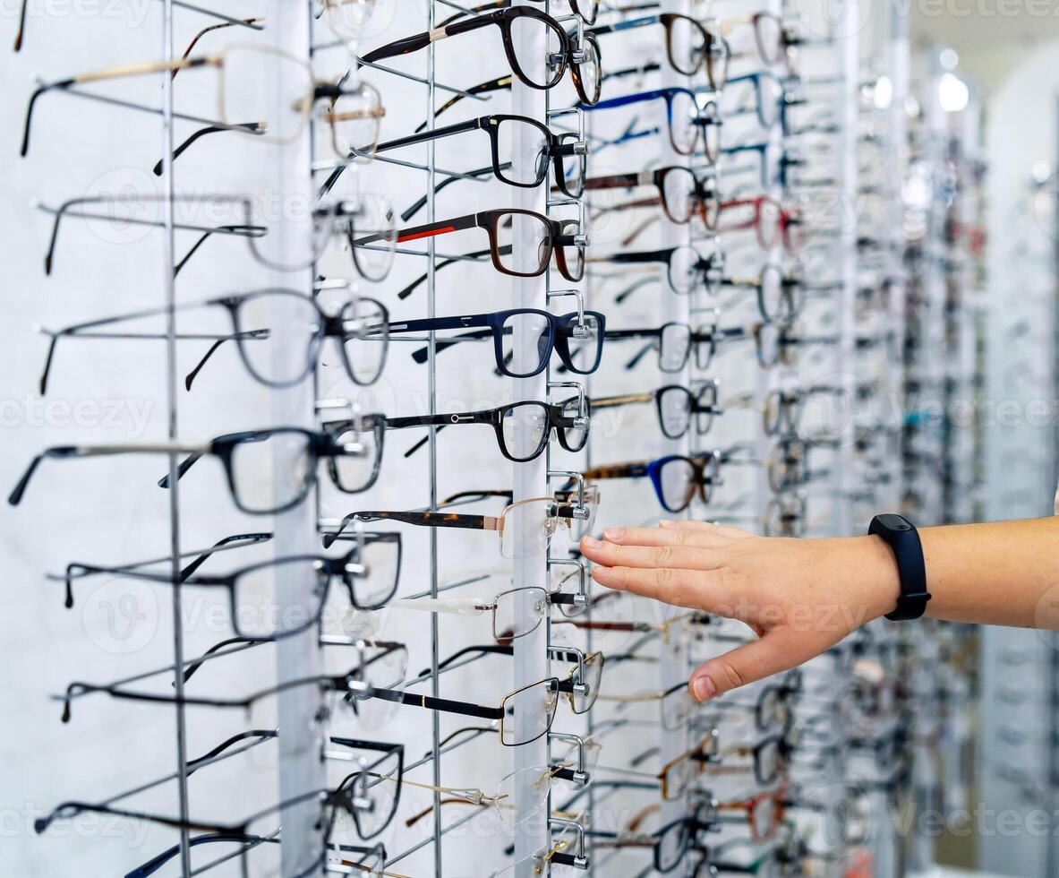 Row of glasses at an opticians. Eyeglasses shop. Stand with glasses in the store of optics. Woman's hand showes glasses. Presenting spectacles. photo