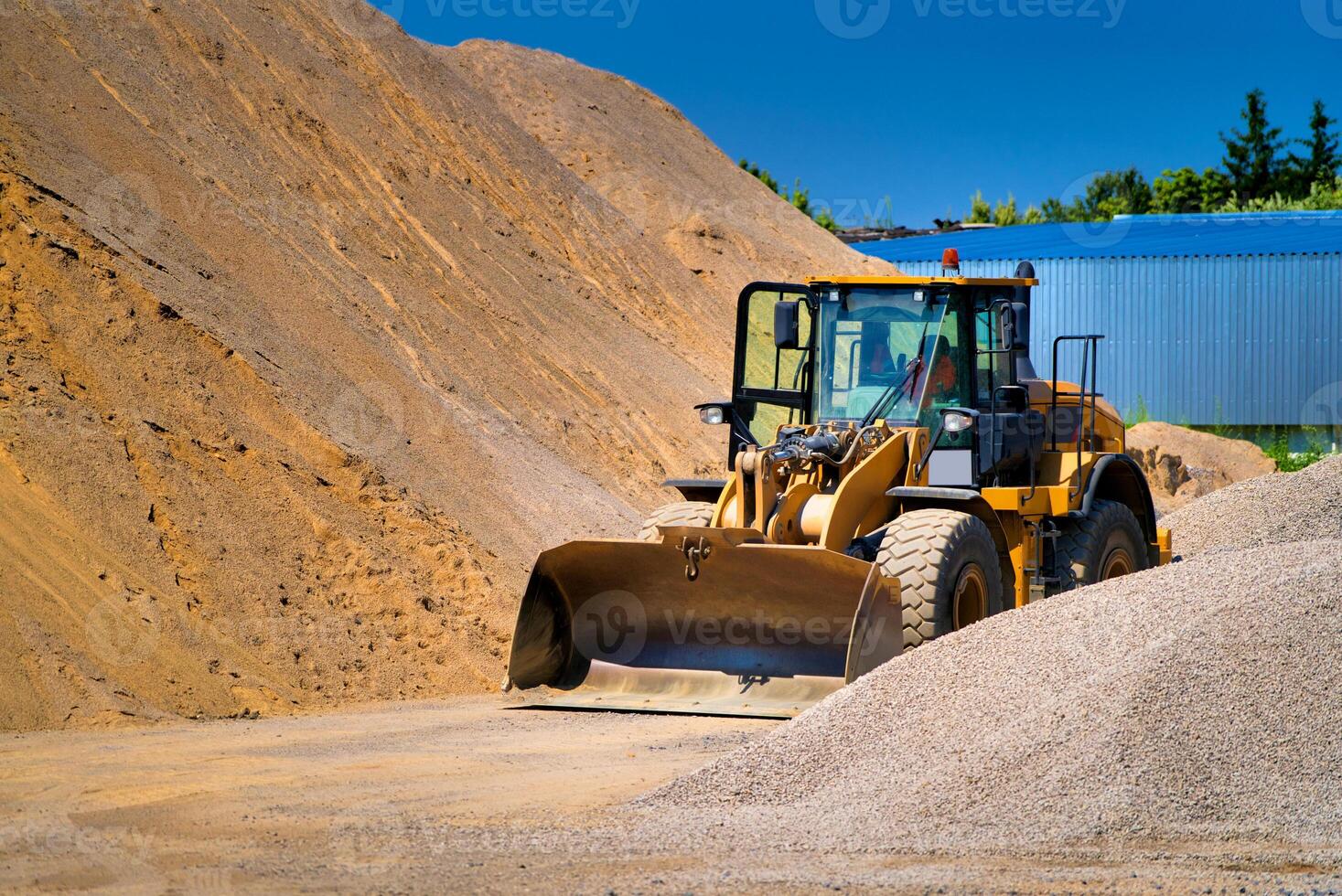 The tractor collects a scoop with gravel. excavator extracts sand and gravel for the concrete mix. Blue sky above. photo