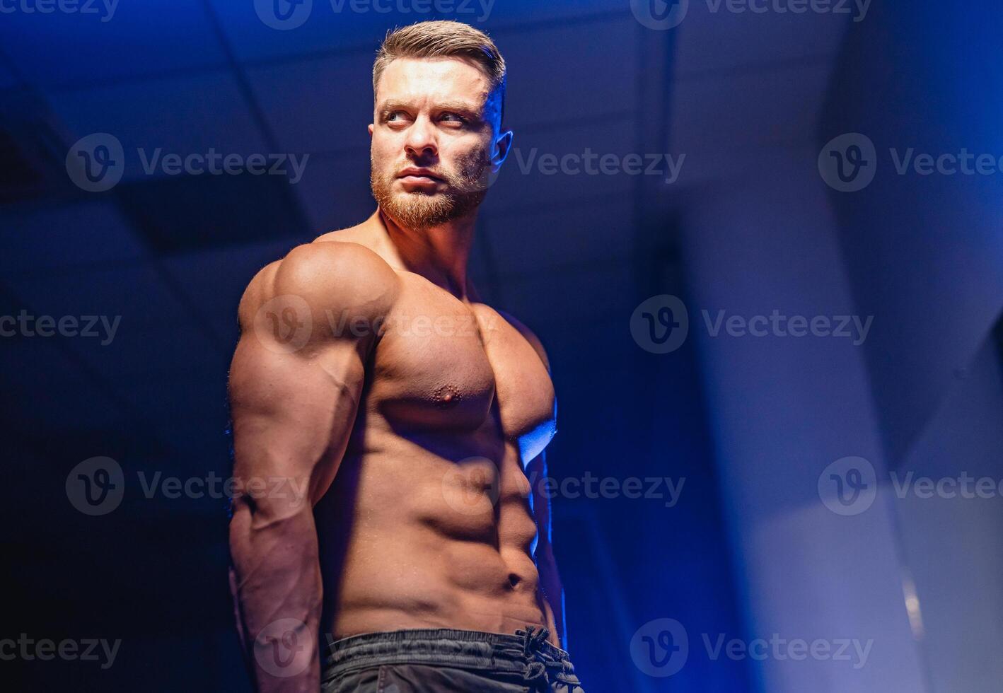 Strong athletic man fitness model torso showing six pack abs. isolated on dark background with blue filter. Closeup. photo