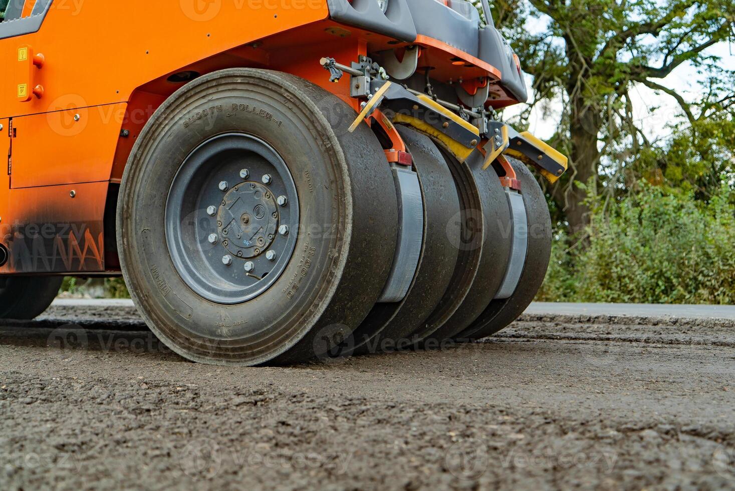 orange steamroller for asphalt with four wheels stands on the road at day photo