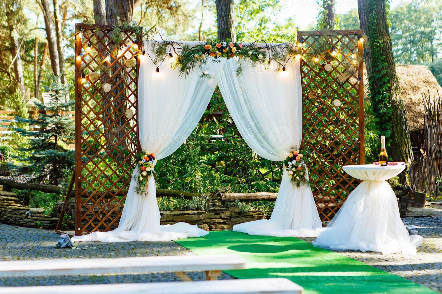 Beautiful place made with wooden square and floral decorations for outside wedding ceremony in wood. Cute wedding arc decorated with flowers and pine branches. photo