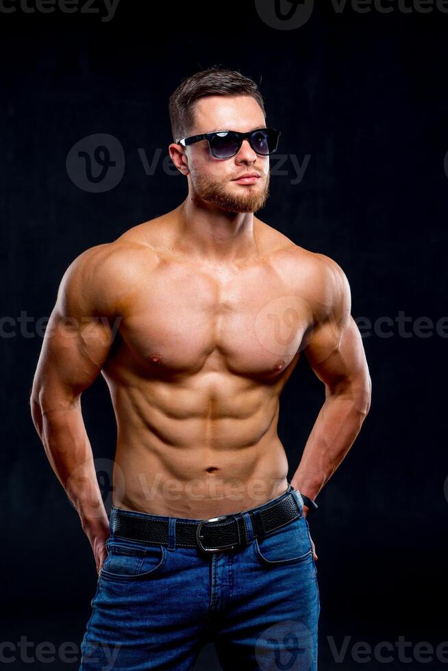 Sexual muscular man posing over dark background. Muscular body and strong abs. Looking at side. Studio shot. photo