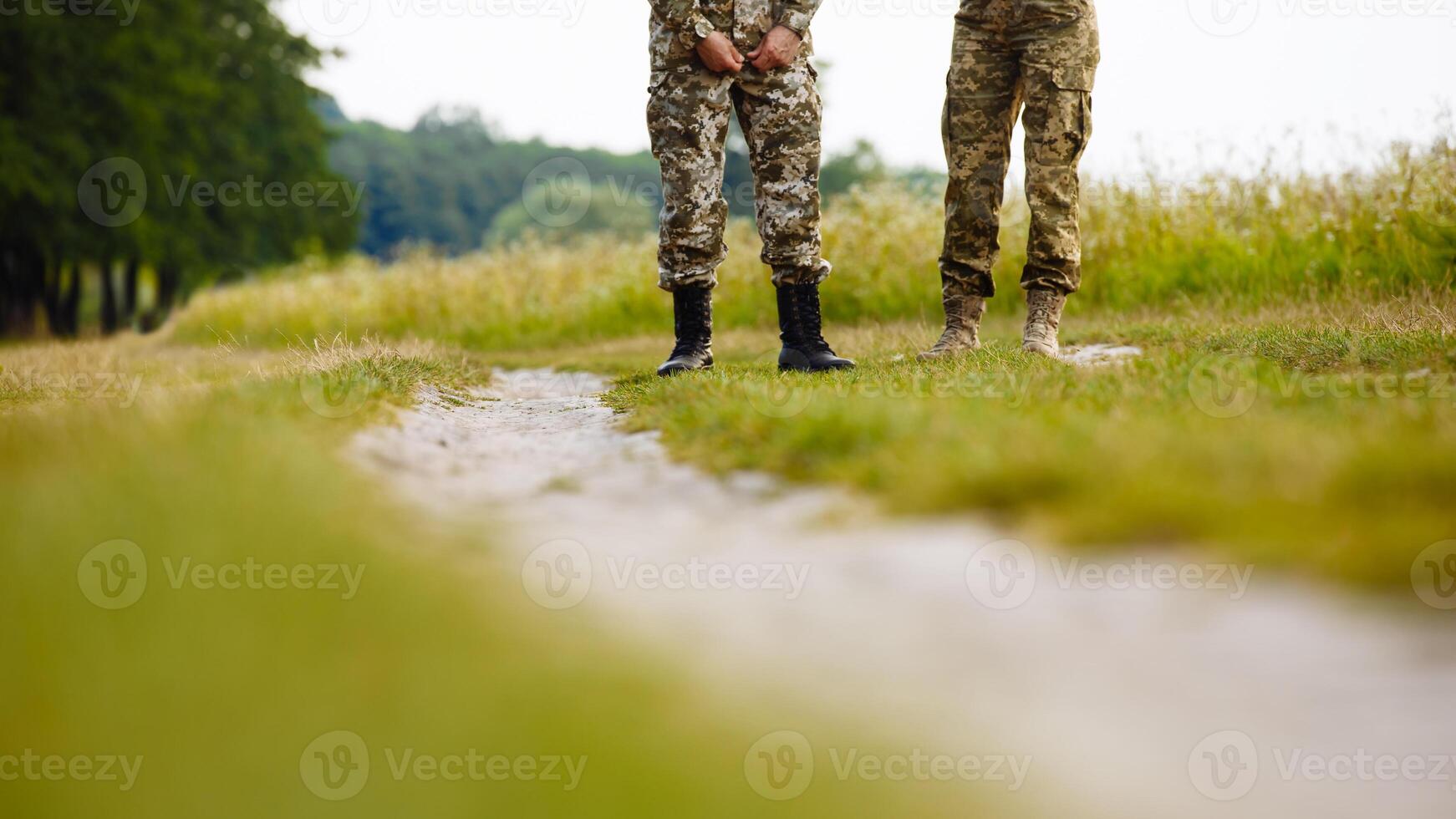 view of the legs of two men in military uniforms in boots near the pathway in the field photo