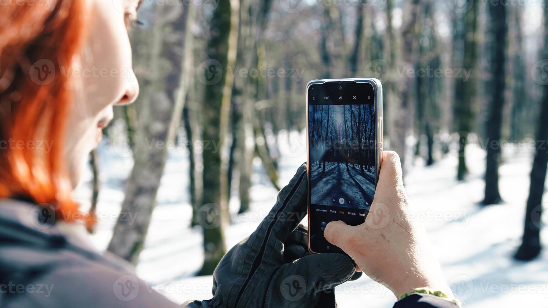 Young woman with gloves taking snow pictures with her phone photo
