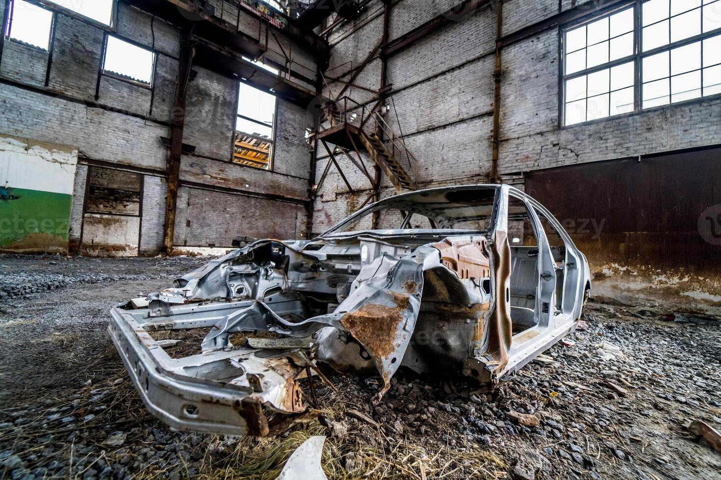 Abandoned in the empty building the old rusty cab of the passenger car. The frame of damaged car on the ground inside the big desolate factory photo