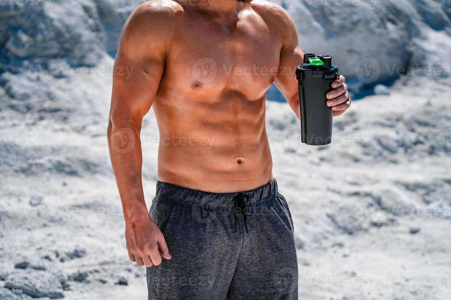 Portrait of a handsome halfnacked bodybuilder man on a mountain with a bottle of water. photo