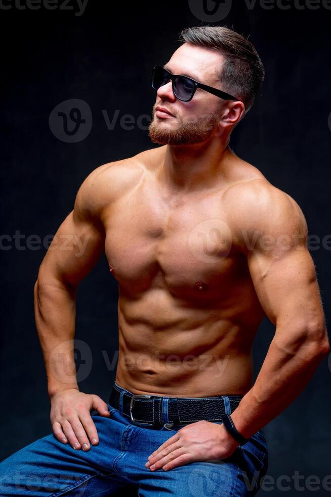 Portrait of a athletic muscular bearded man posing on a black background. Male in glasses showing muscles. photo