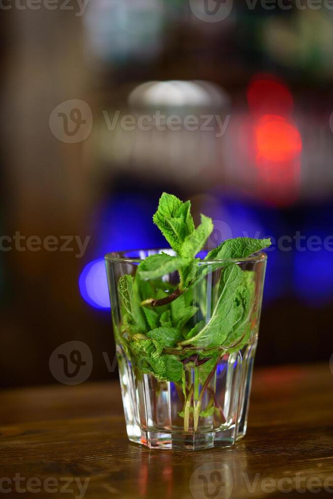 Fresco mojito aislado en borroso antecedentes. el hojas de verde menta en el vaso con agua en de madera mesa. de cerca foto
