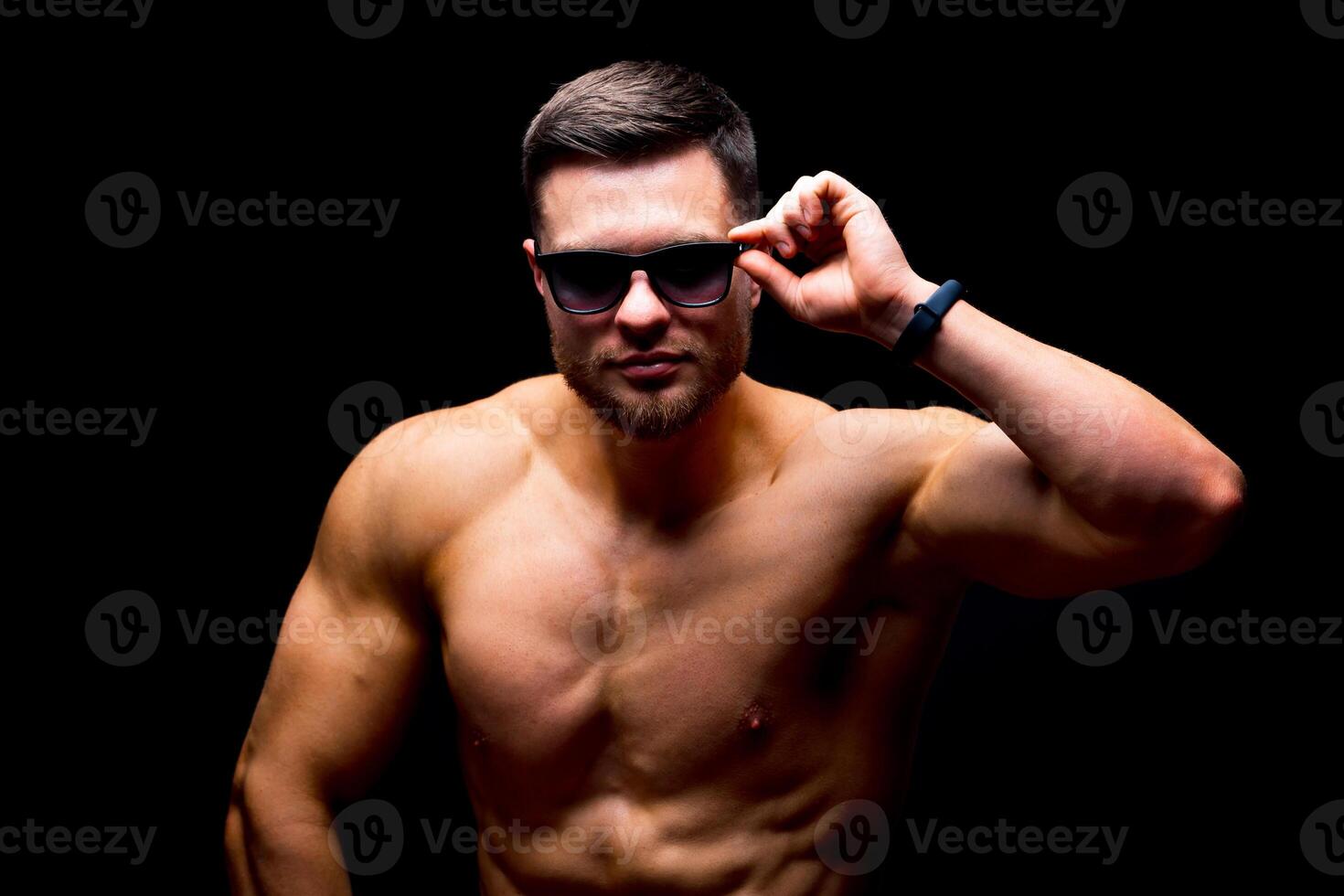 A portrait of a hot handsome strong guy man without a shirt against dark background. wearing glasses. Studio photo. Male beauty concept. Closeup. photo