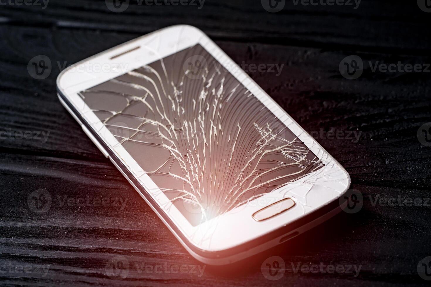 Damaged screen of a broken smartphone isolated on dark background. Crashed mobile phone lying on the floor inside. Close-up photo