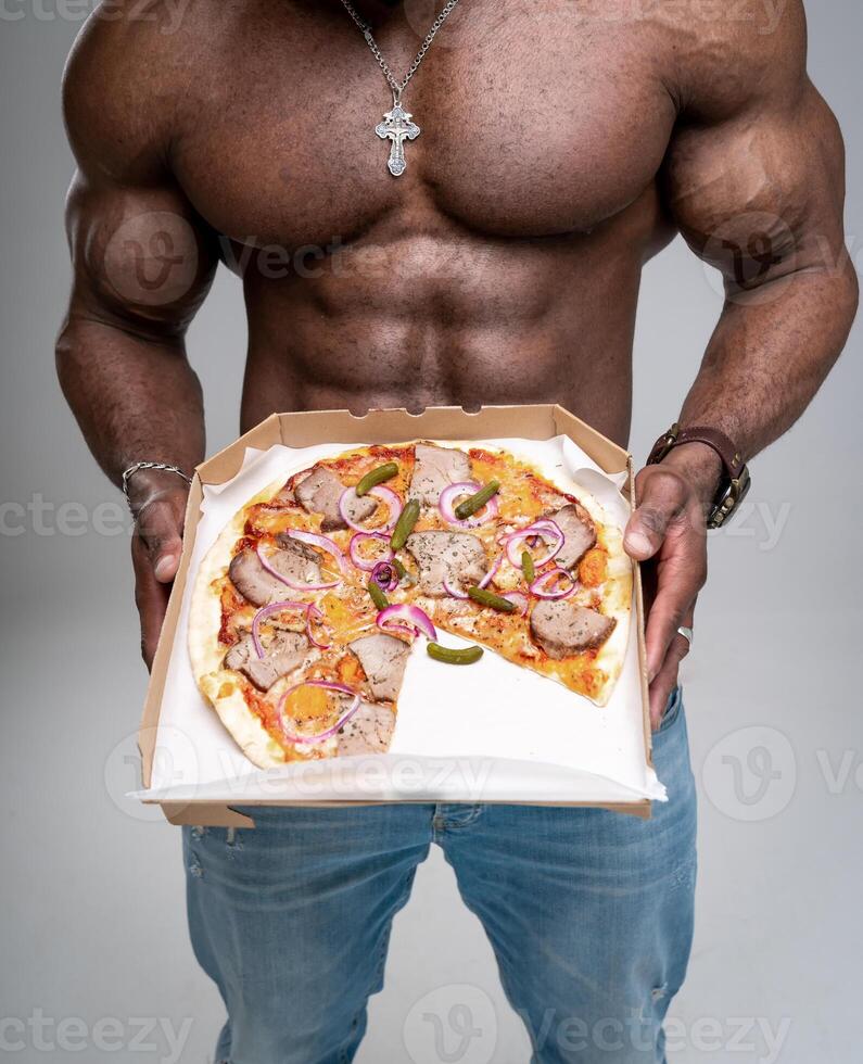 hombre con muscular sexy torso demostración delicioso Pizza. pedazo de Pizza en fuerte manos. atlético mensajero. foto