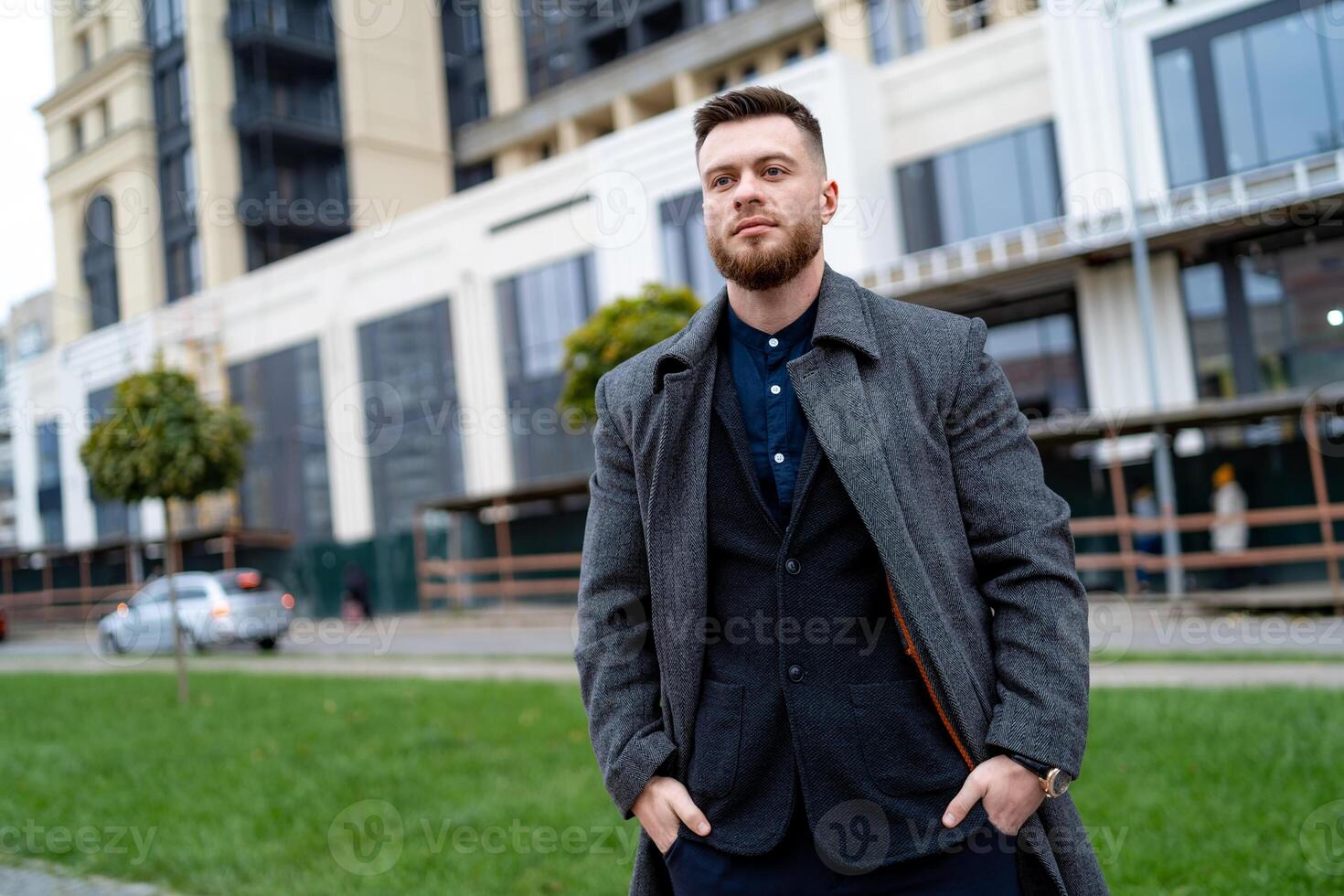 Man in coat is watching beauties of city. Young fashion tourist walking around modern city. Handsome bussinesman staying at urban street. photo
