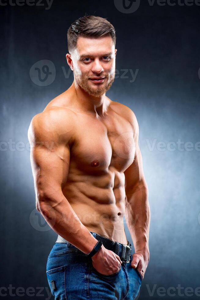 half turned model guy is posing to the camera in the dark grey background. Half waist photo. Strong muscular body. Closeup. photo