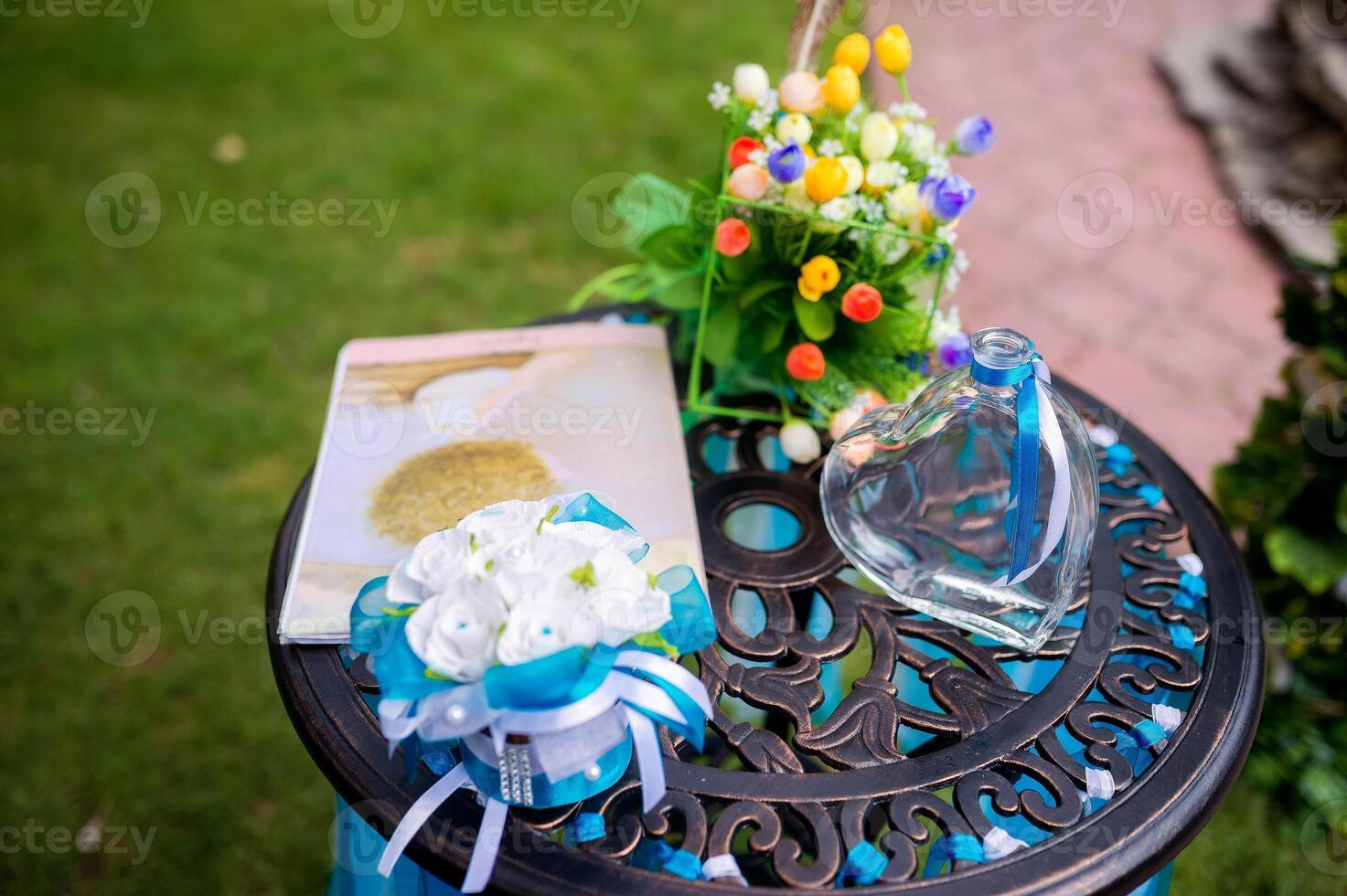 Wedding decoration details. Heart - shaped glass bottle with blue ribbon on a metal table. Closeup. photo