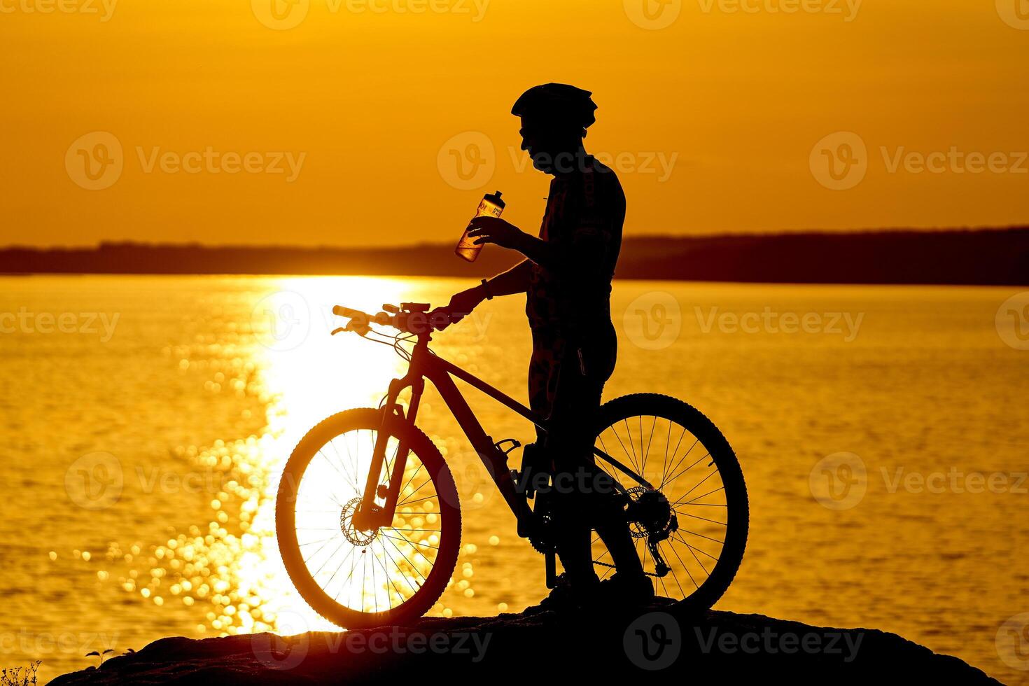 silhouette of a cyclist with sunset background. Orange sky, hobby, healthy habbits. Drinking water while resting photo