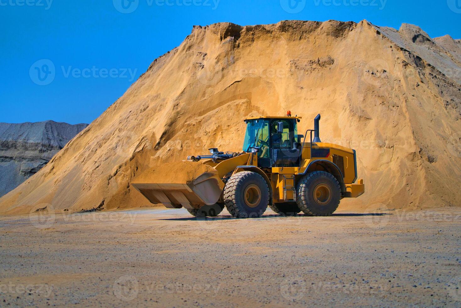 mantenimiento de amarillo excavador en un construcción sitio en contra azul cielo. rueda cargador en montón de arena antecedentes. selectivo enfocar. foto