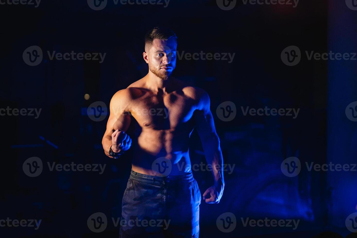 Attractive body builder posing and showing off muscles on dark black and blue background. Filters used. Naked torso. Fitness concept. Closeup. photo