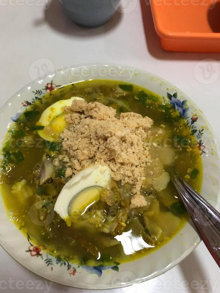 a bowl of Lamongan, Indonesia, chicken soto complete with koya and sliced boiled eggs photo