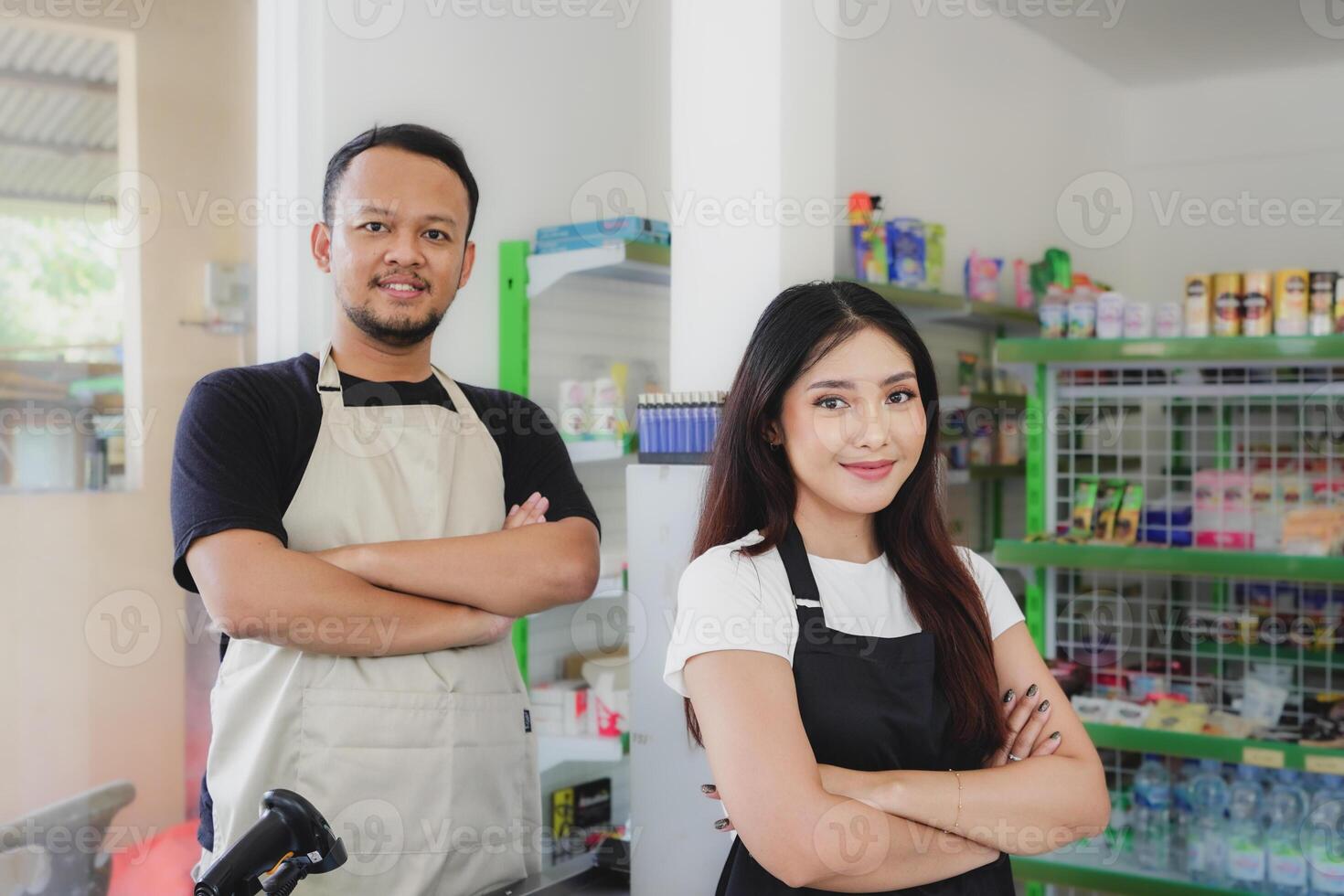 Confident young Asian people as convenience store staff in apron standing with arms crossed smiling to camera. photo