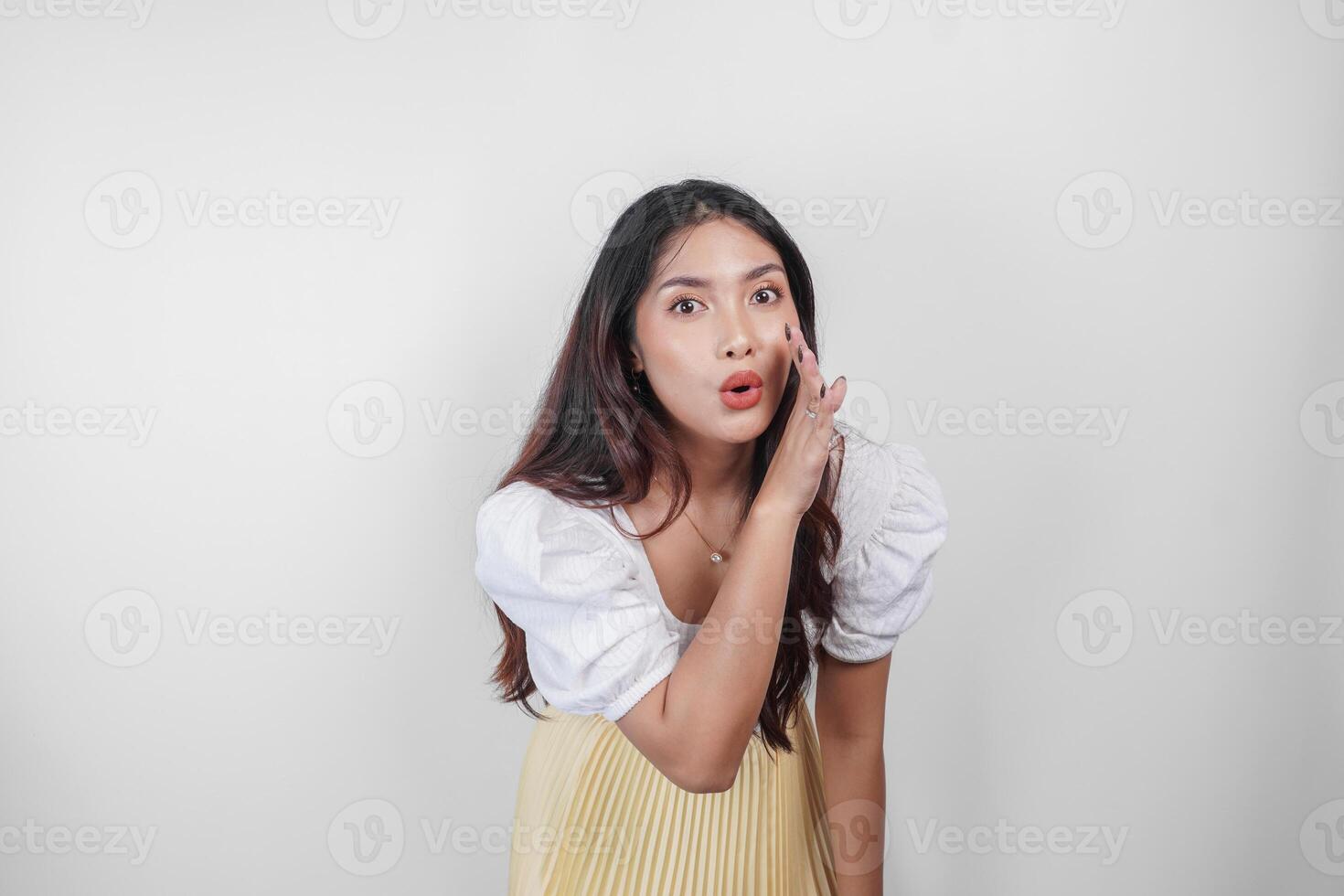 A young beautiful Asian woman is shouting and screaming loud with a hand on her mouth, isolated by white background. photo