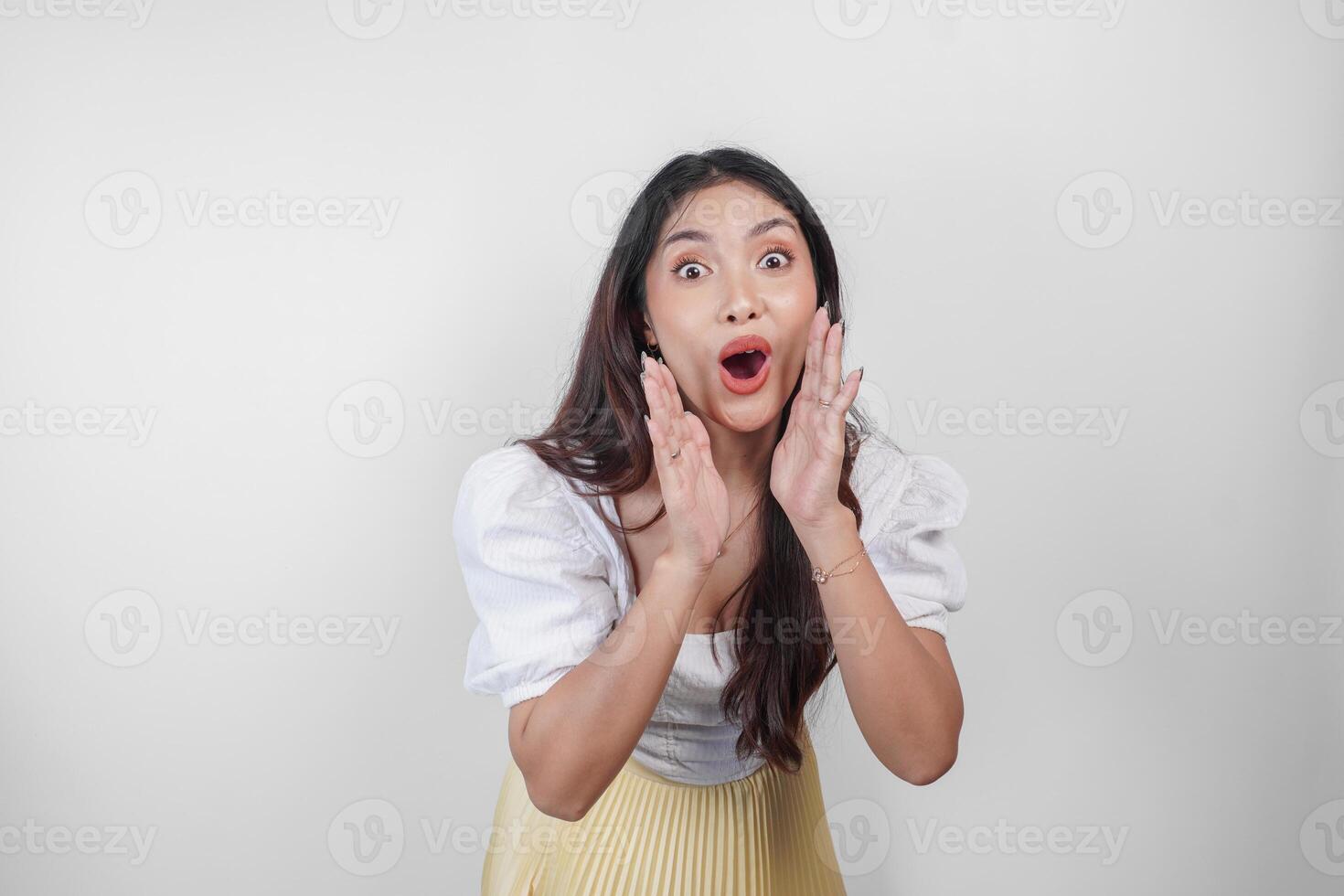 A young beautiful Asian woman is shouting and screaming loud with a hand on her mouth, isolated by white background. photo