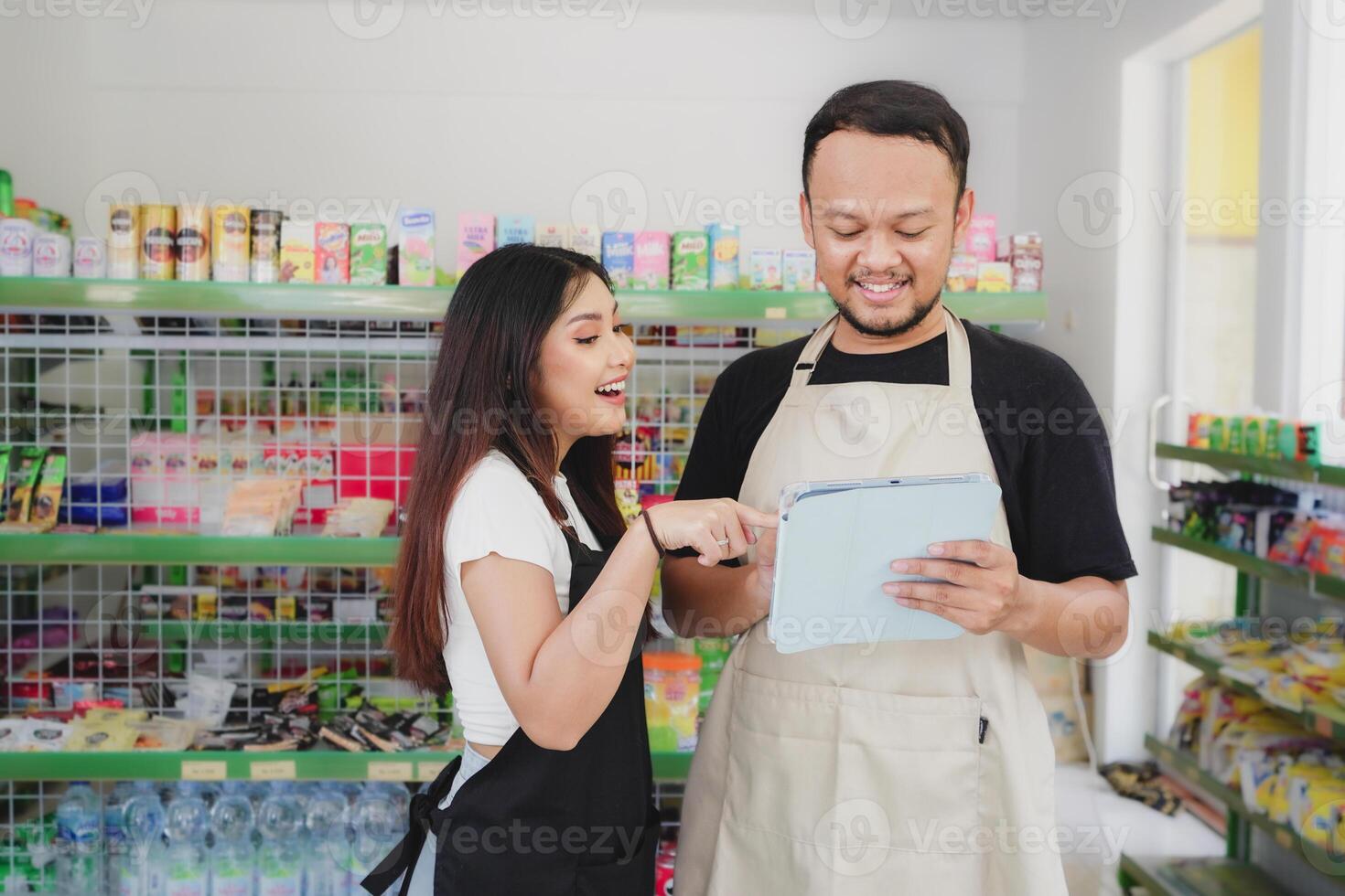 Smiling Asian people holding a tablet, cashier is wearing black and cream apron standing in a groceries or convenient store photo