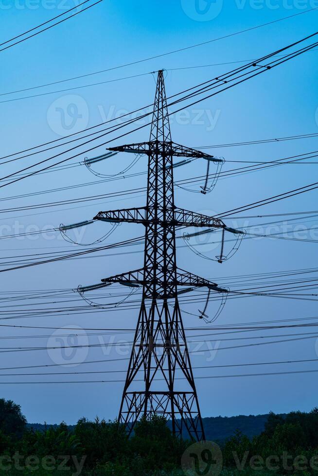 Single high voltage tower on the background of blue sky after sun set. Numerous wires of electricity power stations at the backdrop of twilight. Dark blue sky crossed by the heavy cables. photo