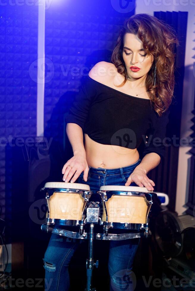 Closeup of beautiful emotional expressive cool young brunette. Talanted musician woman with long curly hair standing in recording studio playing drums with hands. photo