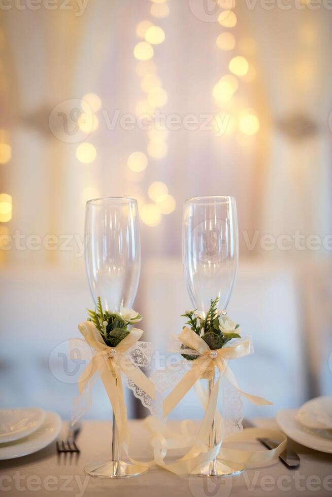 Two empty wedding champagne glasses with creamy bows and flower decor on the table. Glasses for groom and bride. photo