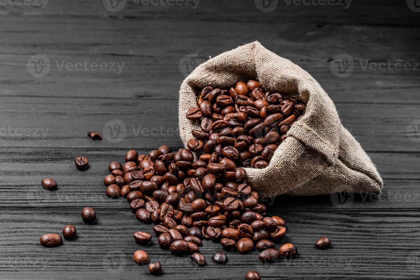 Fresh roasted coffee beans falling out the sack on the wooden surface. Brown coffee beans scattered from bag on the table photo