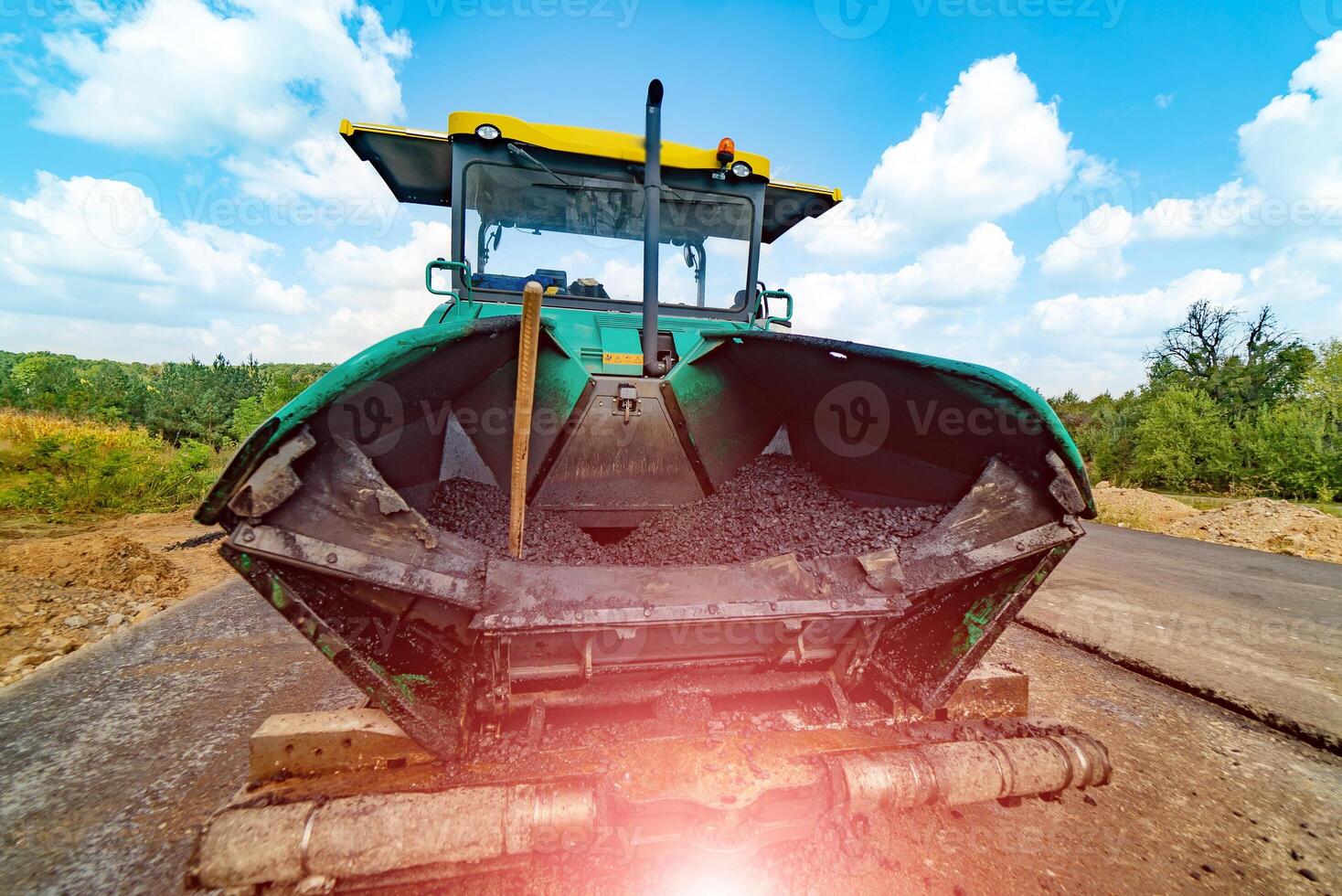 Tracked paver laying fresh asphalt pavement on top of the gravel base during road construction photo