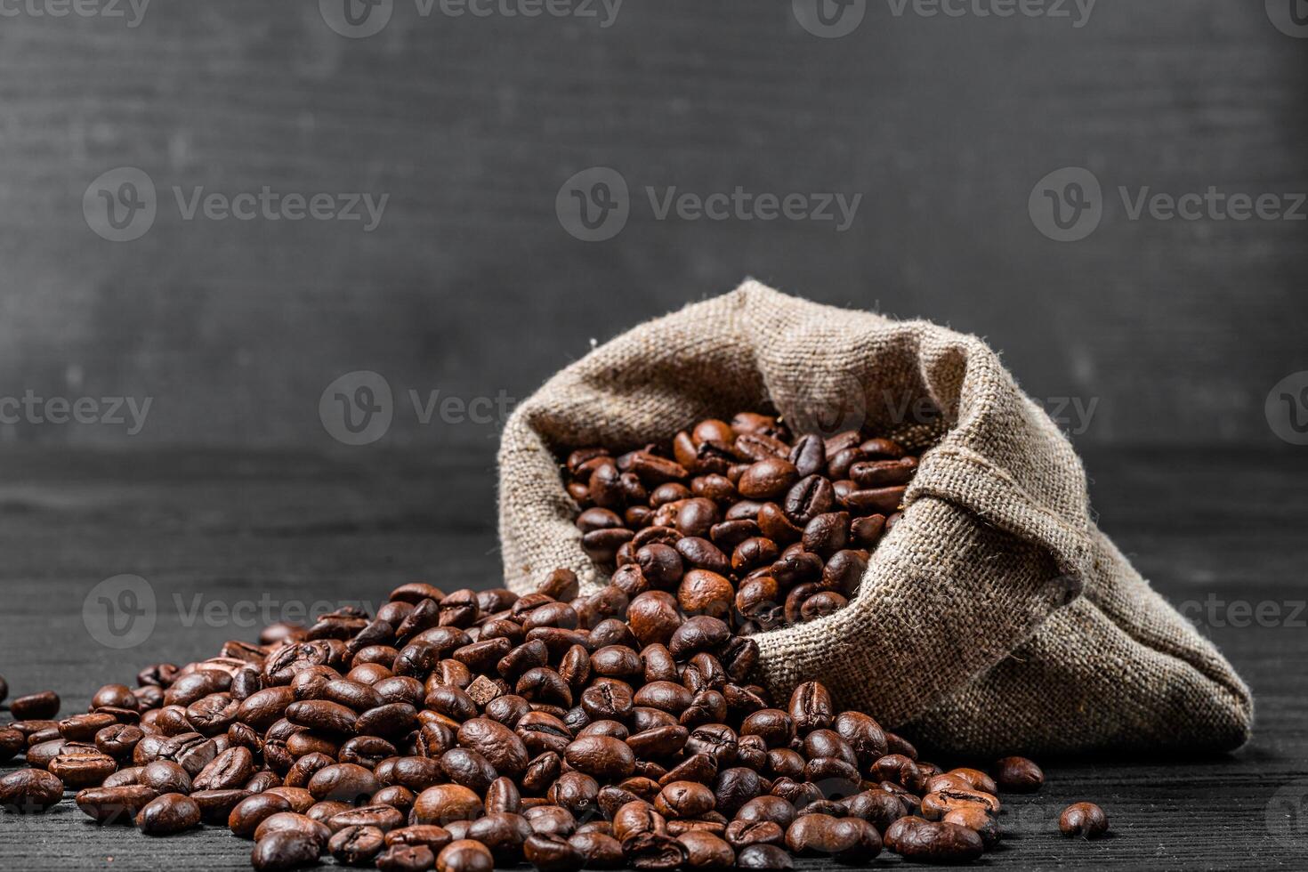 Bag with scattered coffee beans isolated on the black background. Coffee beans lying on the dark surface falling out the sack. Close-up photo