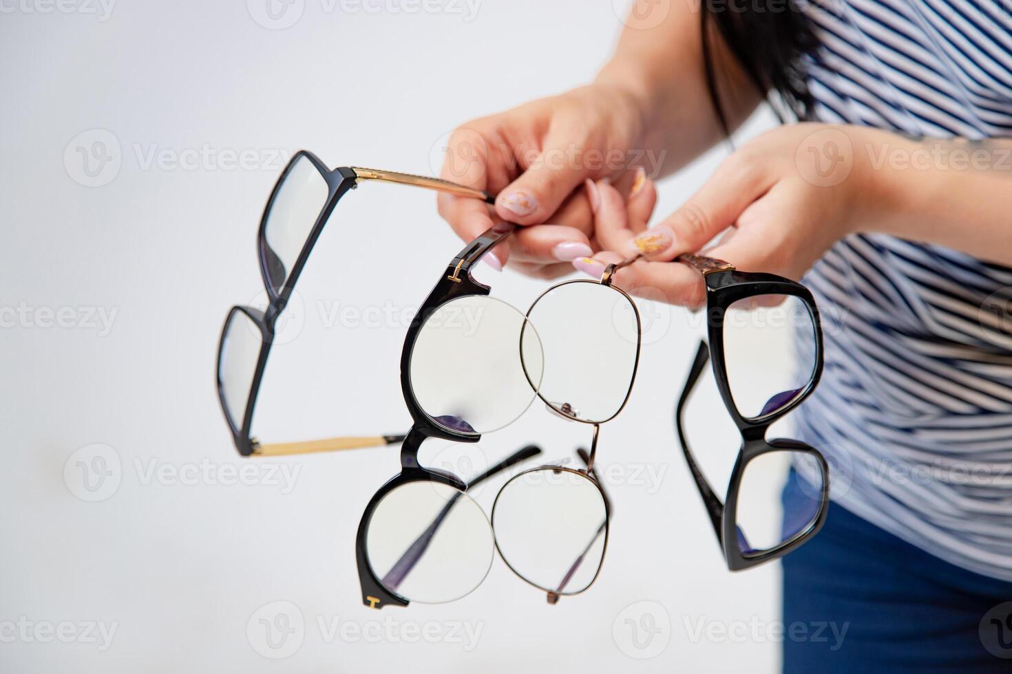 woman shows four pairs of eyeglasses to choose from on a white background in the studio. Close-up photo