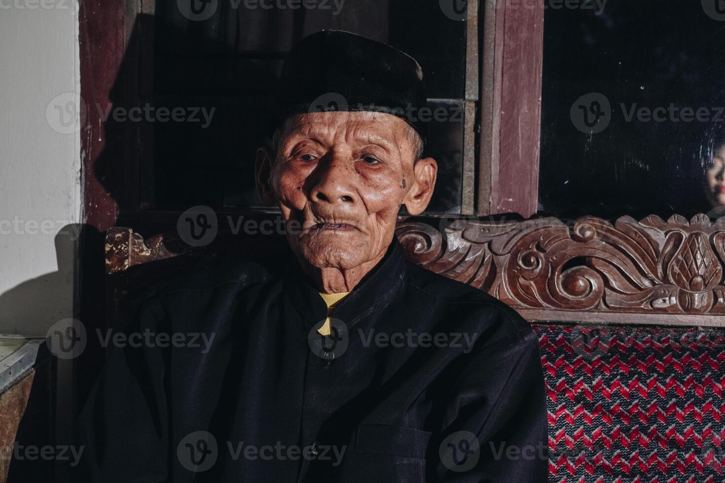 Thoughtful senior Asian man sitting on home sofa, looking away with thoughts, thinking over future retirement, planning, dreaming photo