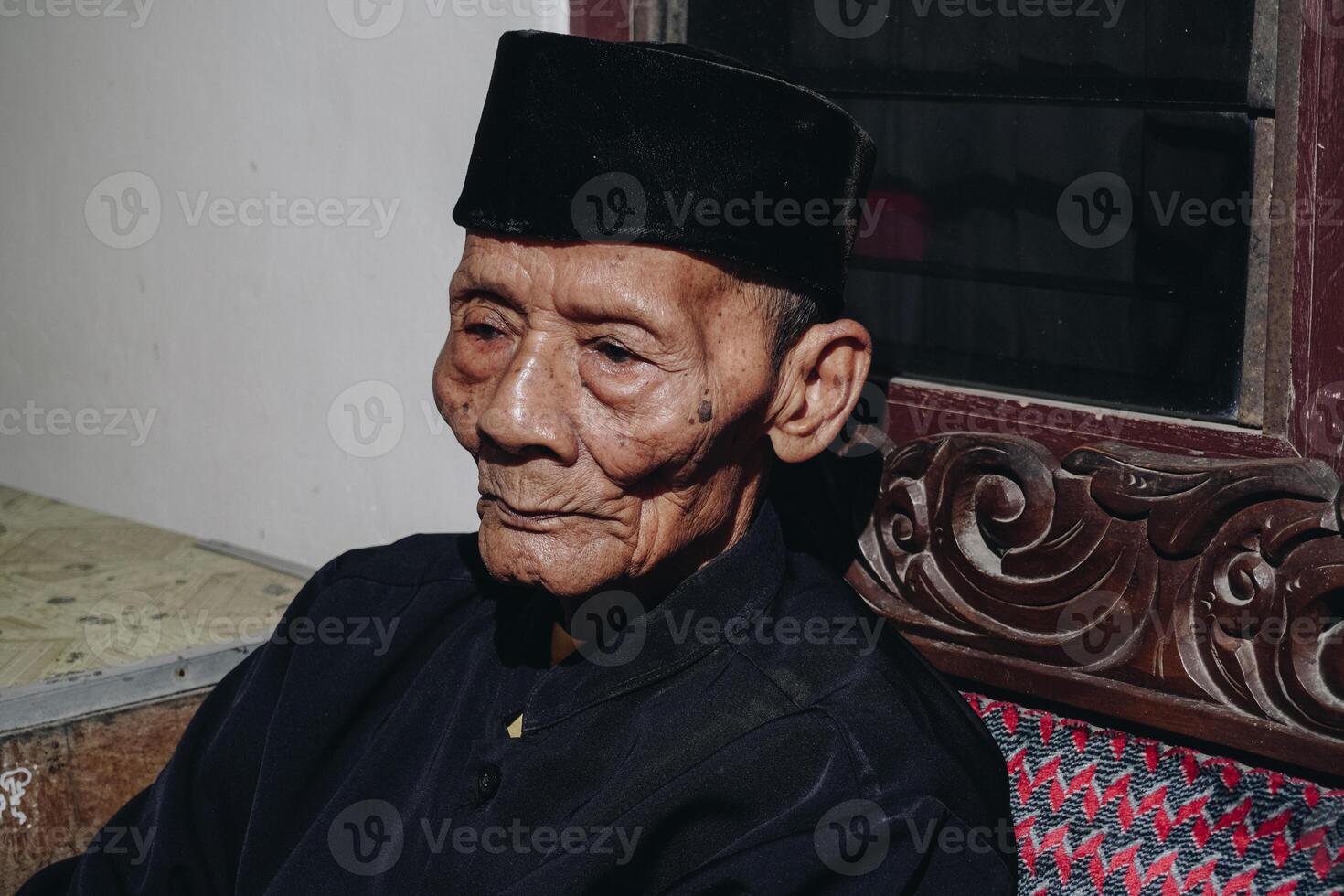 Thoughtful senior Asian man sitting on home sofa, looking away with thoughts, thinking over future retirement, planning, dreaming photo