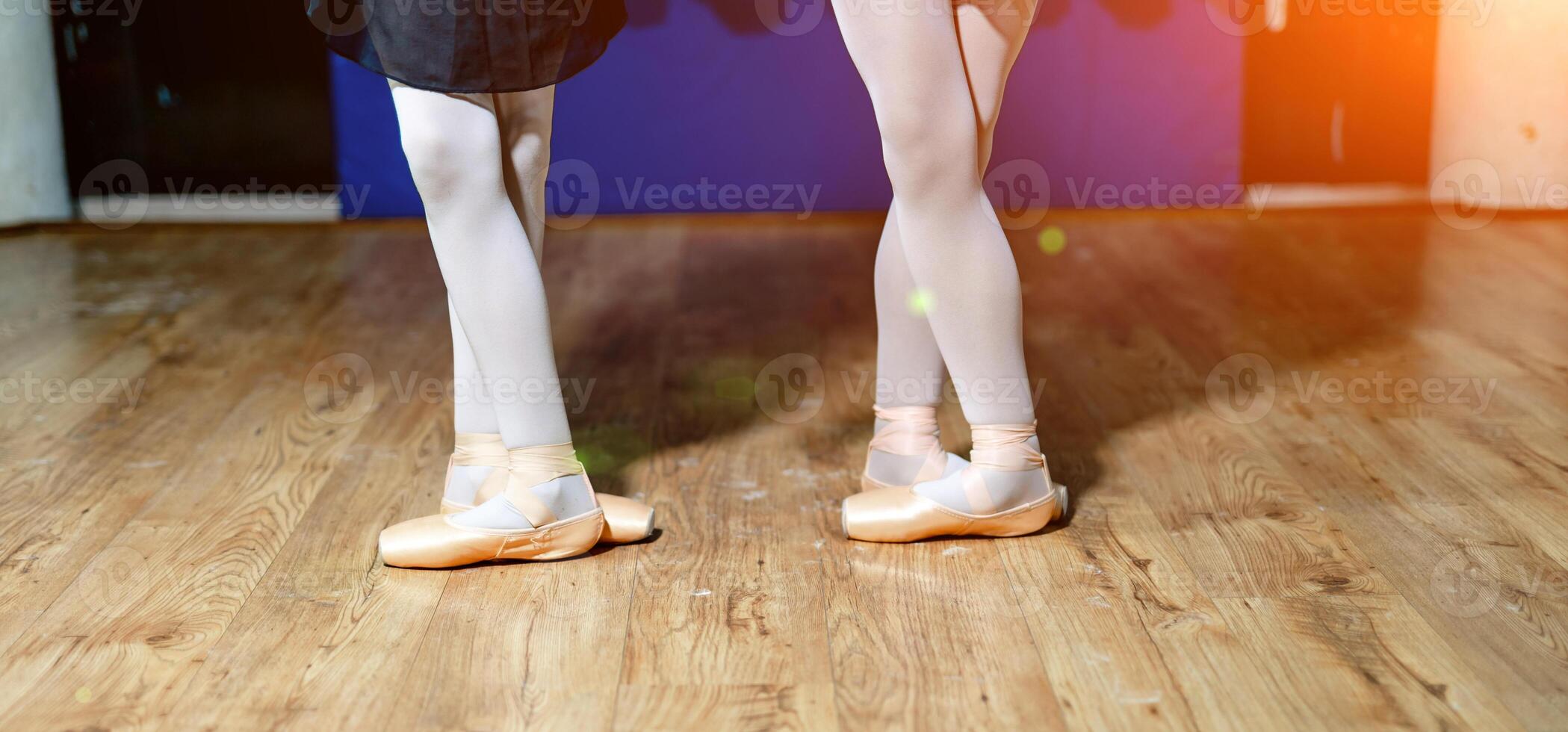 The legs of two young ballerinas in white tights and pointes performing a dance on wooden floor in a studio. Young ballerinas legs in standing in ballet position. photo