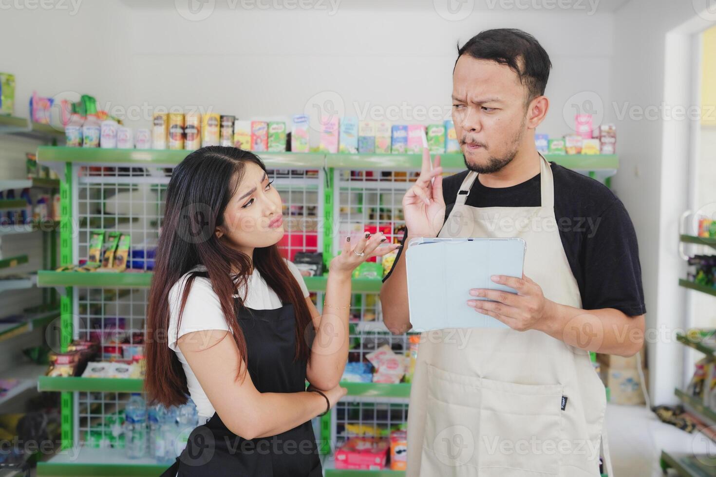 Thoughtful Asian people holding a tablet, cashier is wearing black and cream apron standing in a groceries or convenient store photo