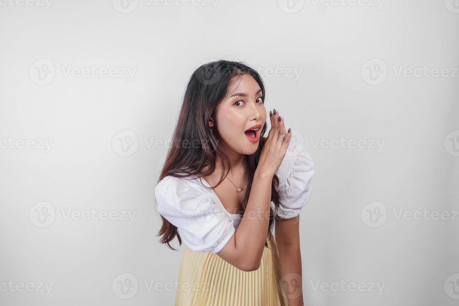 A young beautiful Asian woman is shouting and screaming loud with a hand on her mouth, isolated by white background. photo