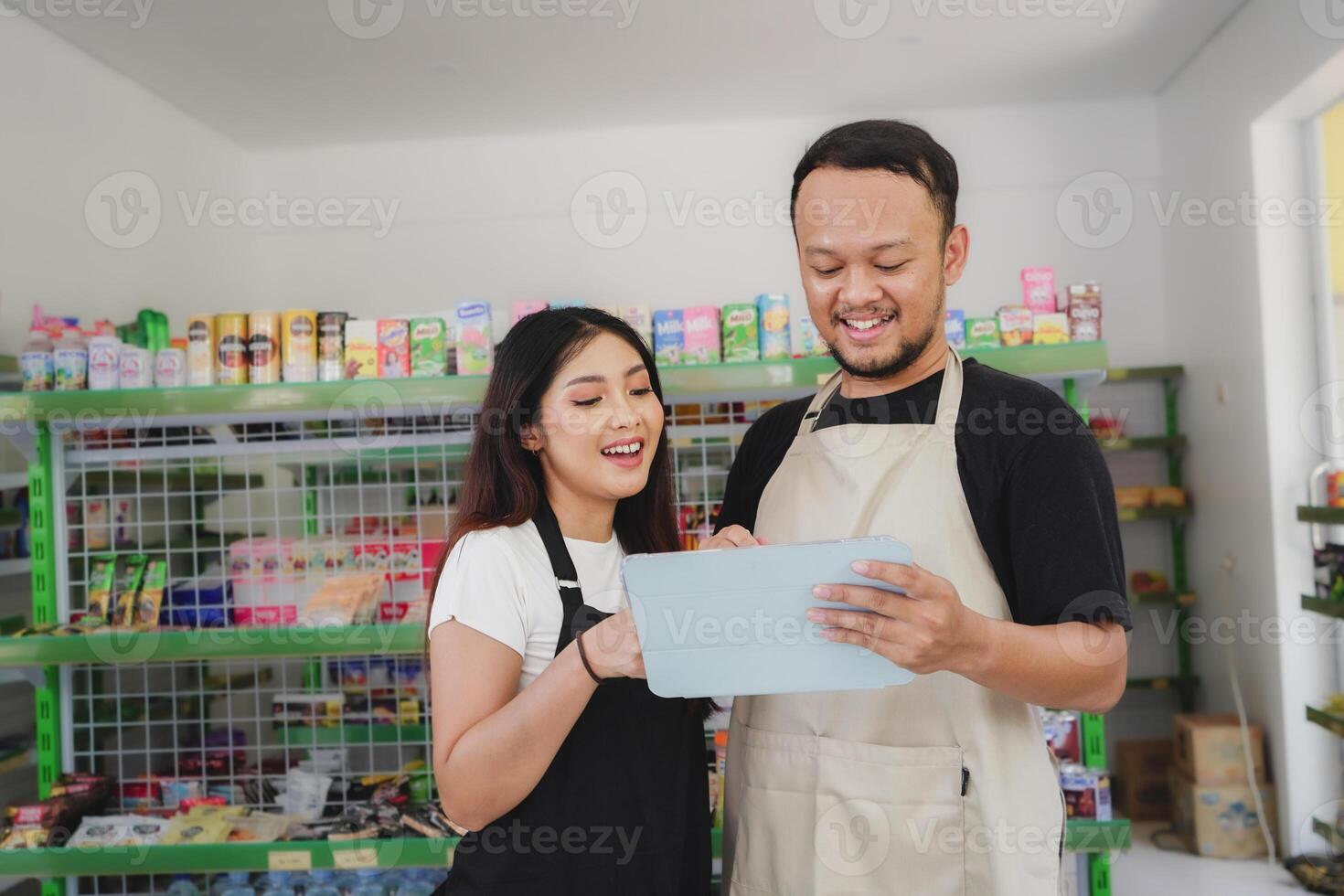 Smiling Asian people holding a tablet, cashier is wearing black and cream apron standing in a groceries or convenient store photo