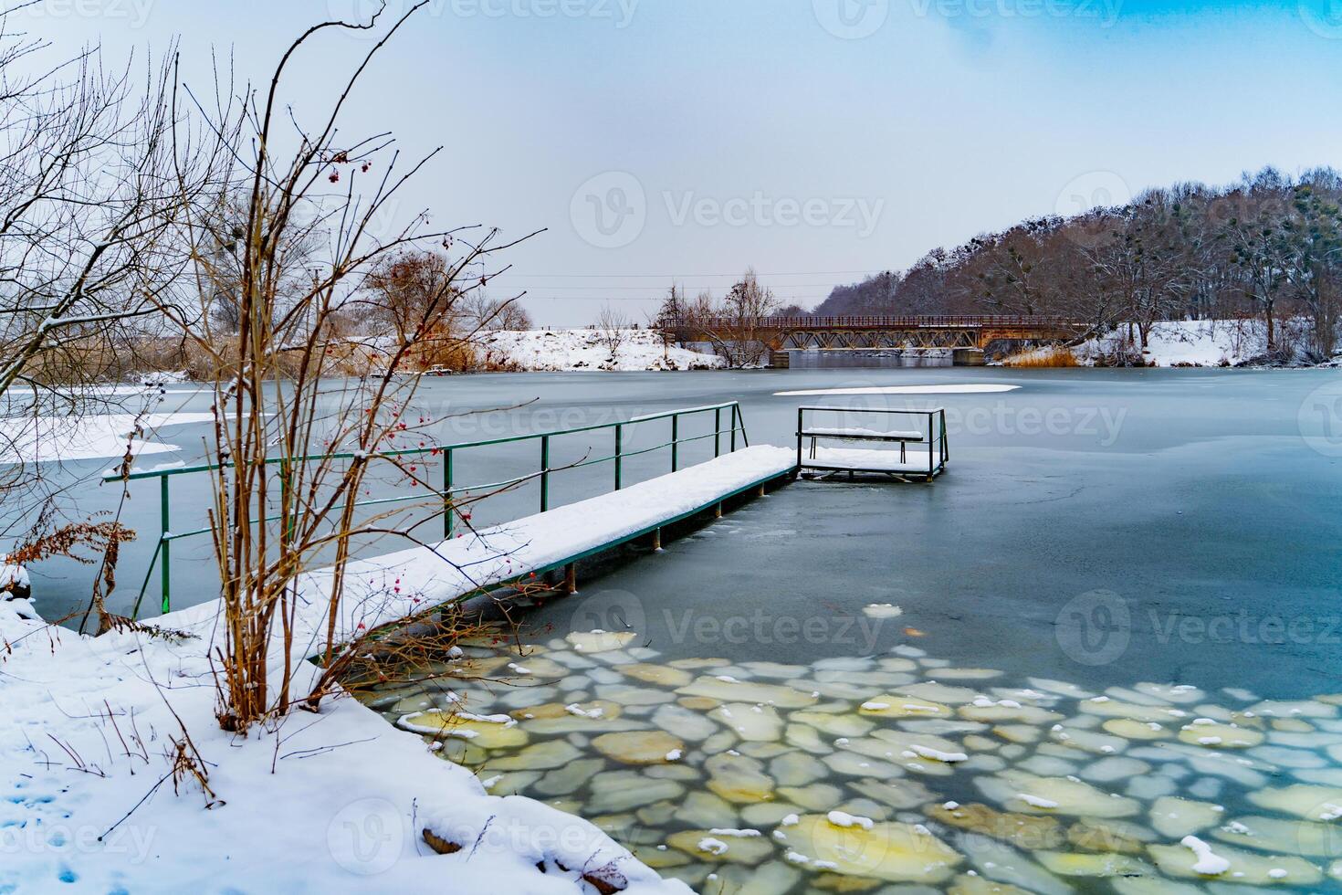Beautiful landscape with frozen river and bridges over it in winter. Picture of nature with snow and the river covered with ice near the forest. photo